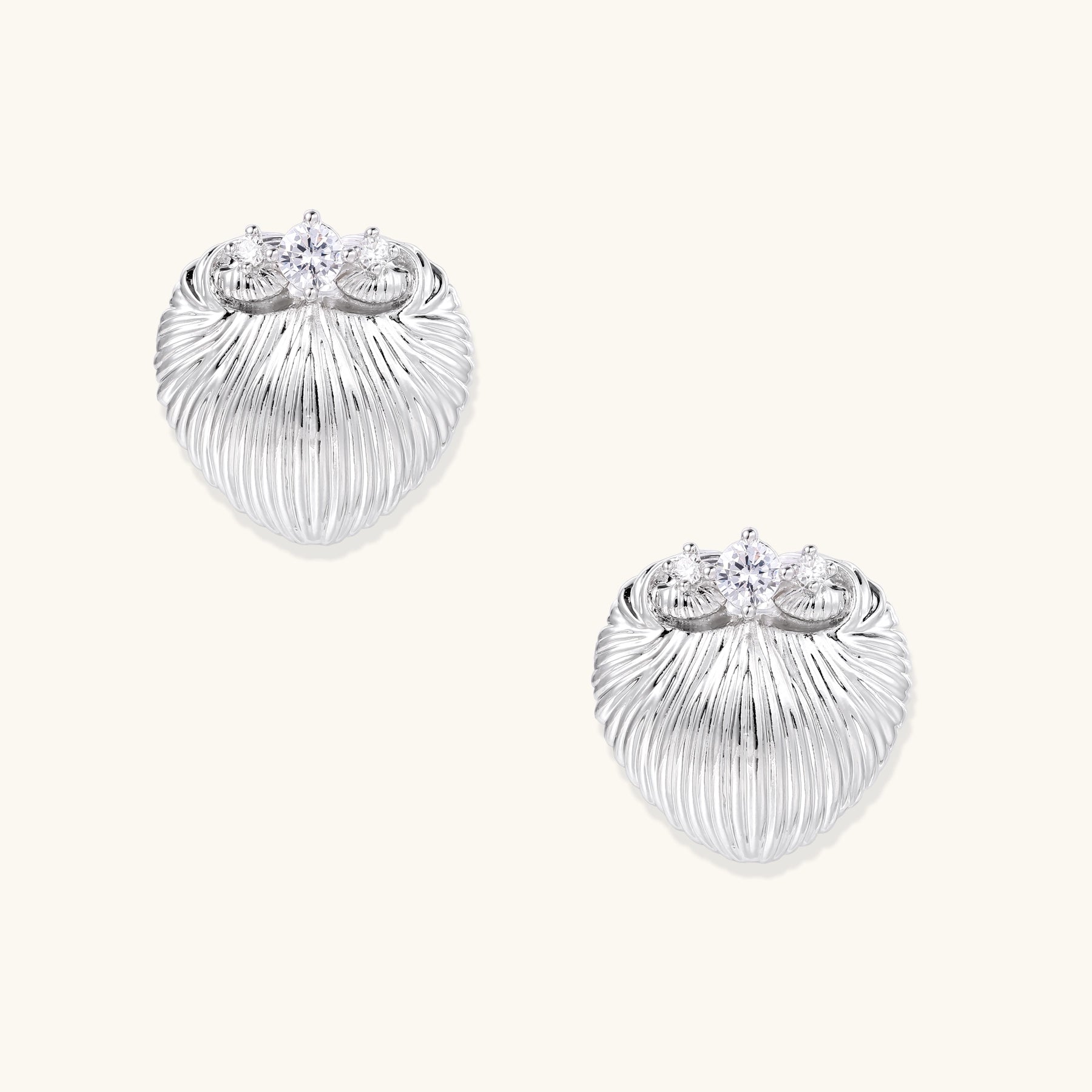 Pair of gold-plated heart-shaped earrings with vertical ribbed texture and sparkling zirconia stones at top on white background.