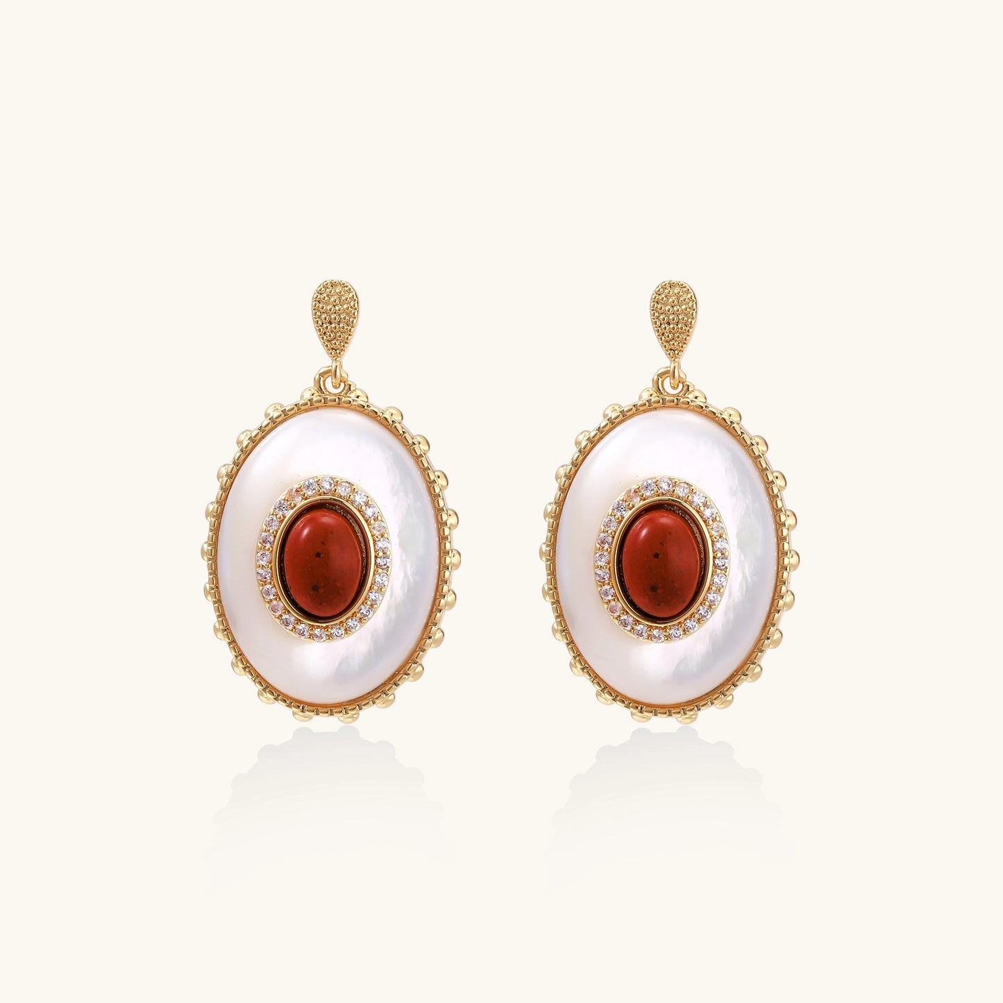 Gold-plated drop earrings with oval mother-of-pearl stones, central red gemstones, and crystal accents on white background.
